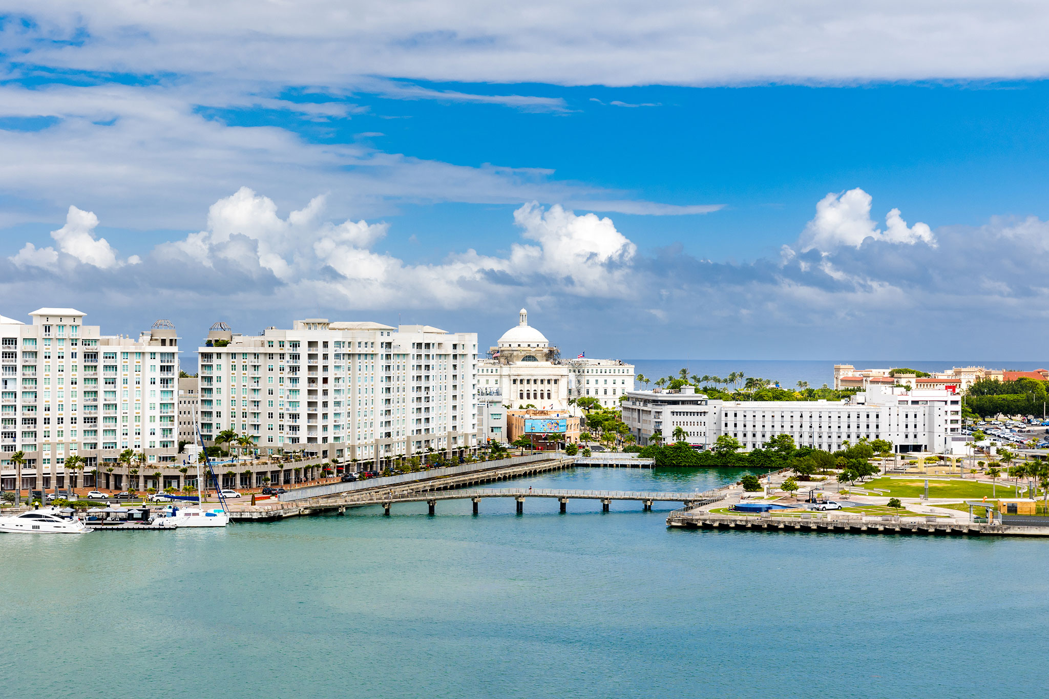 Aerial view of waterfront buildings and a marina in a tropical city under a cloudy sky.