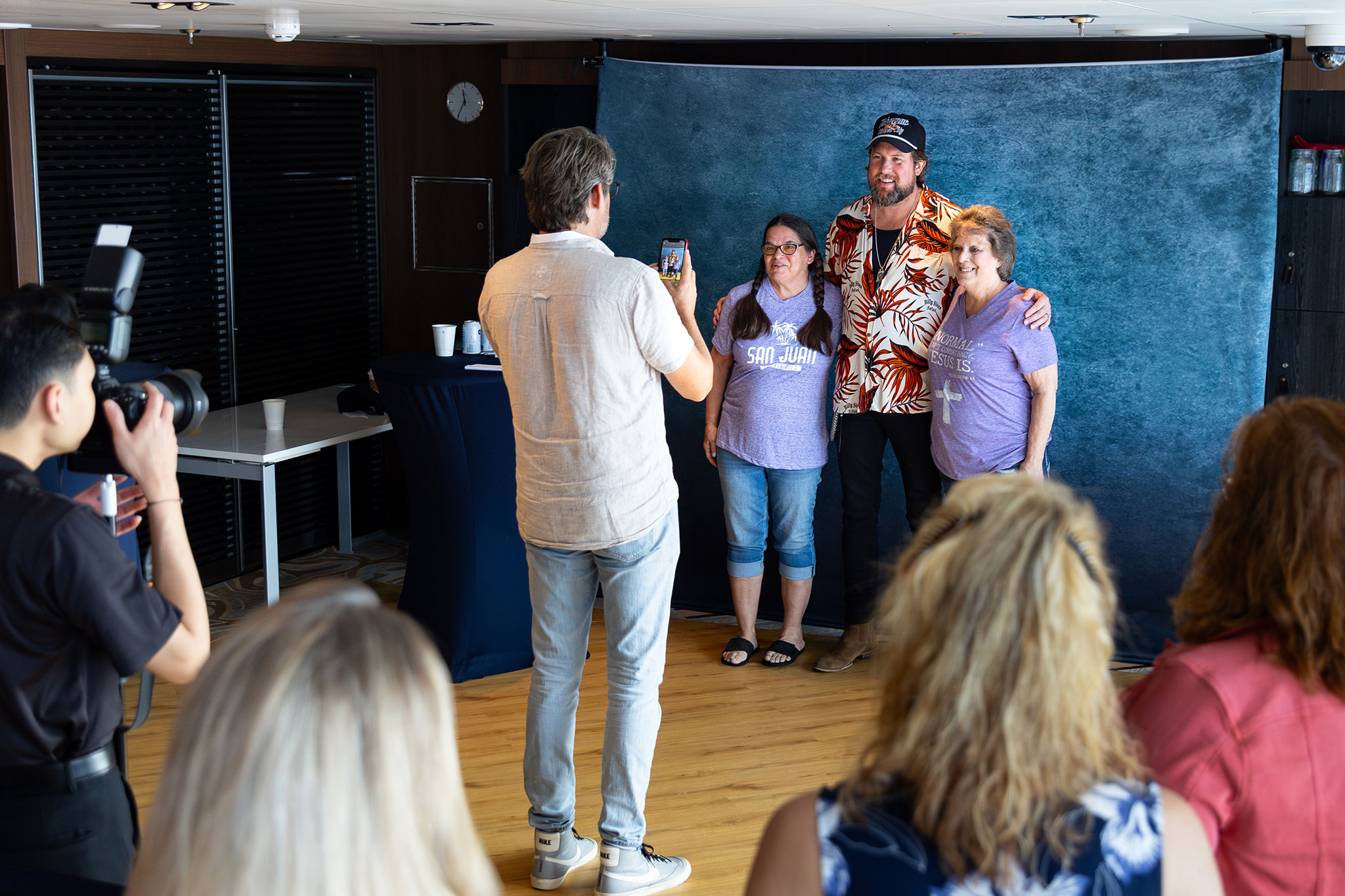 Fans posing for a photo with a tall man at a meet-and-greet event, with a photographer capturing the moment.