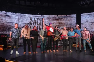 Zach Williams with a group of musicians onstage during opening night, taking a bow with guitars and other instruments in front of a rustic backdrop.
