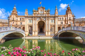 Bright flowers frame a scenic view of twin bridges and tiled details that shine under blue skies at Plaza de Espana.